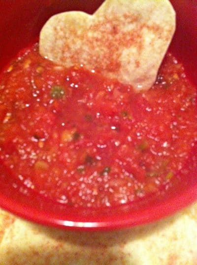 Heart shaped tortilla cracker in a bowl of salsa.