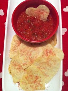 White tray with red salsa in a red bowl and heart shaped tortilla crackers.