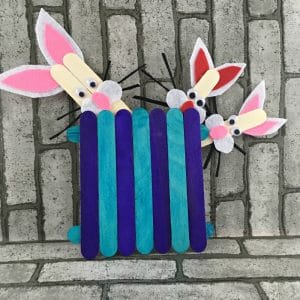 Aqua and purple popsicle stick fence with three popsicle stick bunnies peeking out the top of the fence.