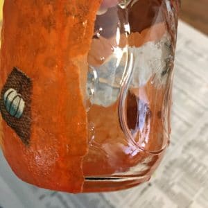 Mason jar with one side clear and one side orange modge podge cover.