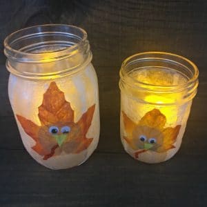 Two illuminated mason jar with turkeys on front of mason jar.