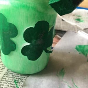 Green mason jar being painted with shamrocks.