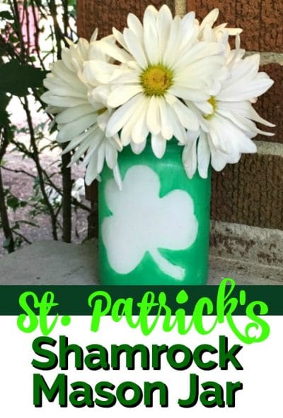 Dreen mason jar with a shamrock on the outside and white daisies.
