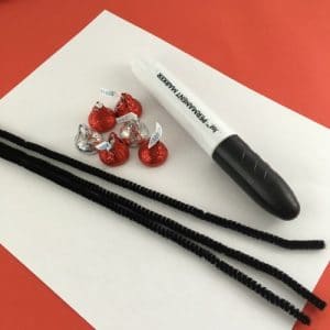 Craft supplies: white paper, black sharpie, black pipe cleaners, hershey kisses red and silver.