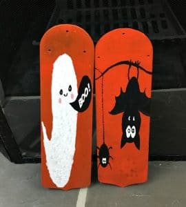 Two orange painted fan blades: one with a white ghost and one with black bats as Halloween door hangers.