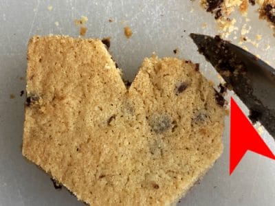 Chocolate chip cookies being shaved with knife into shape of a heart. Red arrow points to edge of top of heart.