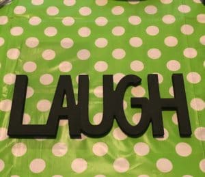 Laugh in wood letters painted black on a green and white polka dot background.