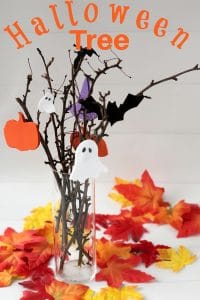 Halloween Tree made from branches, halloween ornaments made from paper in a clear glass vase surrounded by leaves.