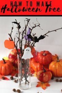 Halloween Tree made from branches, halloween ornaments made from paper in a clear glass vase surrounded by leaves.