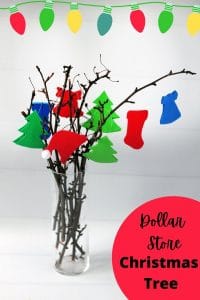 Glass vase with branches. Green Christmas tree ornaments, red bell ornaments hanging off branches.