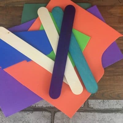 Variety of popsicle sticks fanned out on top of purple, orange, green foam paper.